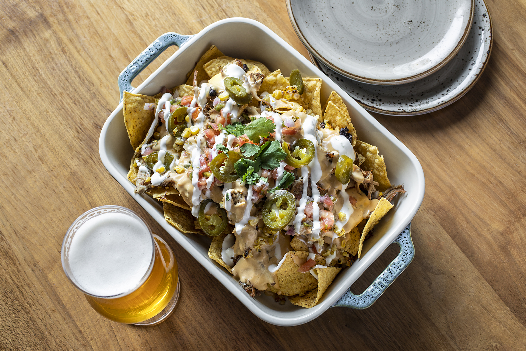 nachos in casserole dish with two extra plates and a glass of beer