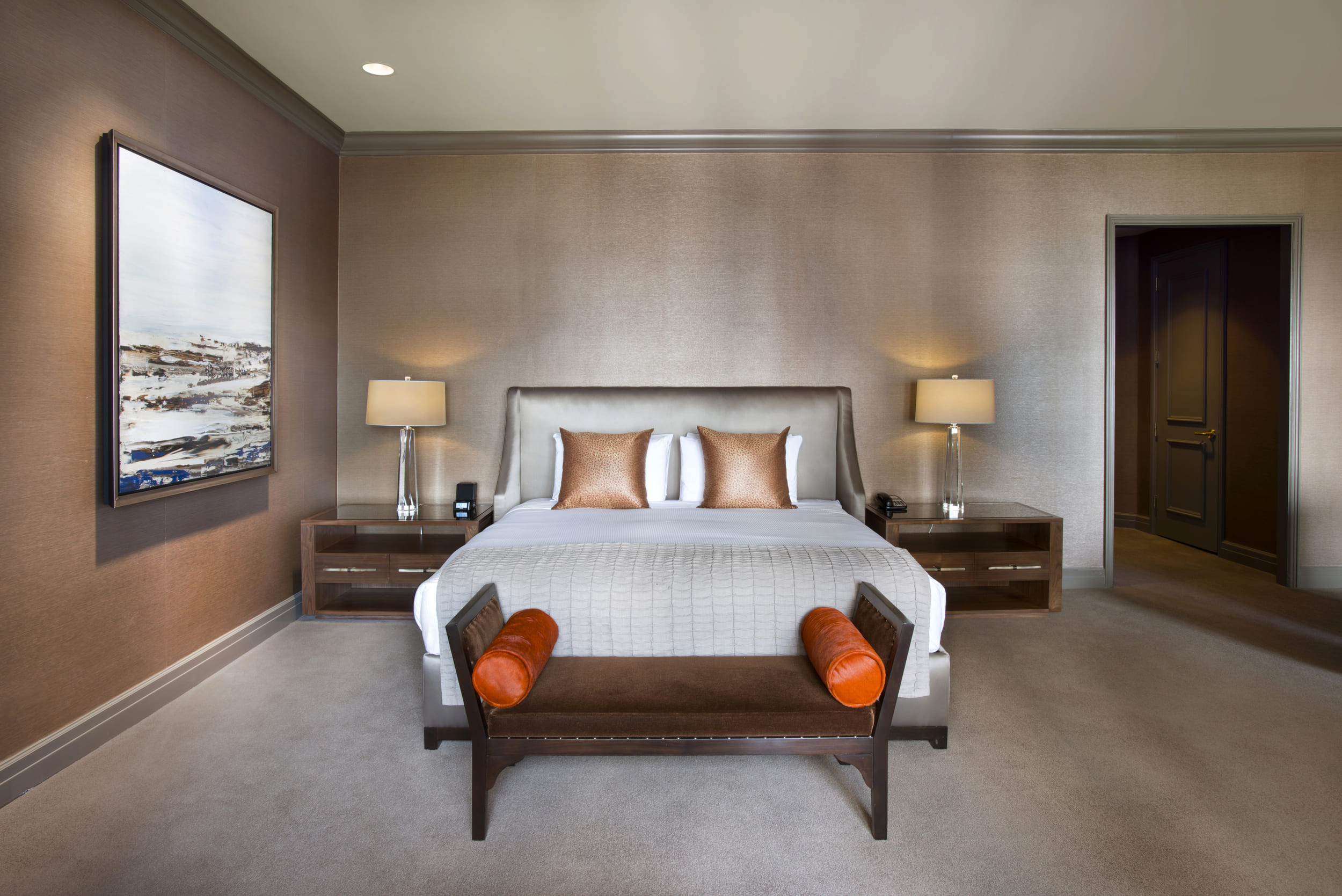 bed with orange pillows and bench at the foot
